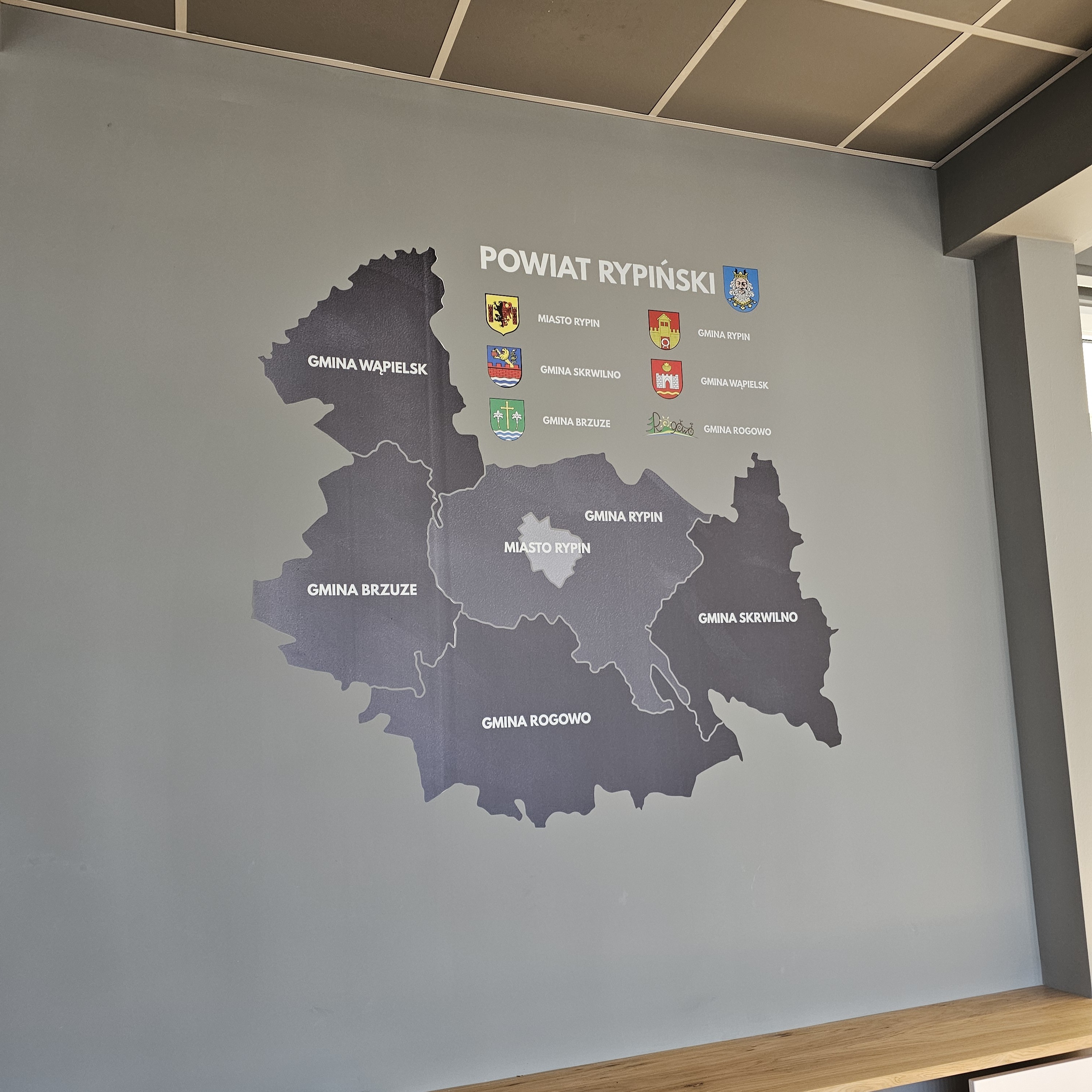 Mapa powiatu rypińskiego z herbami gmin wydrukowana na ścianie starostwa